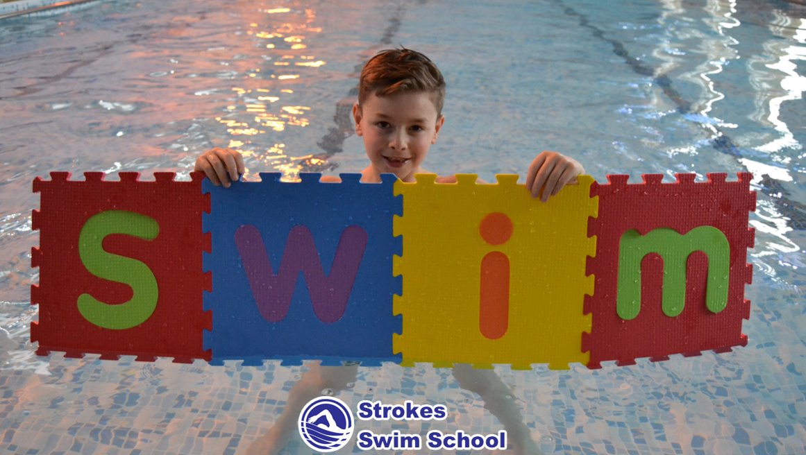 Boy holding colourful SWIM letters in the swimming pool
