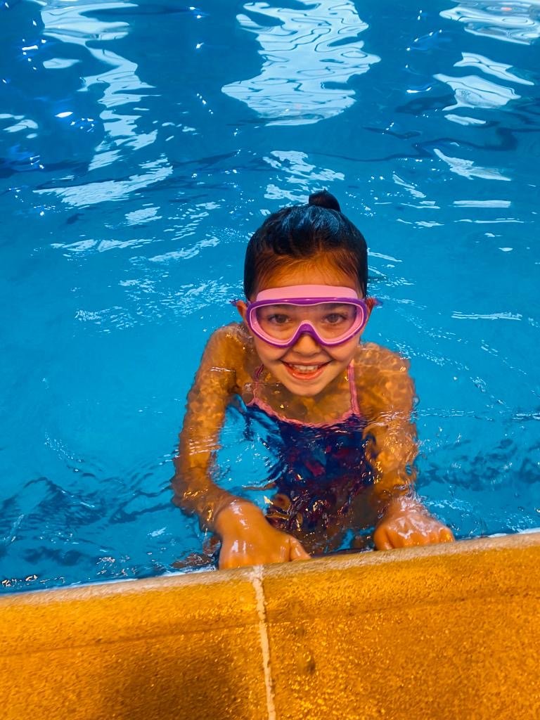 Girl with pink goggles smiling at swimming pool edge