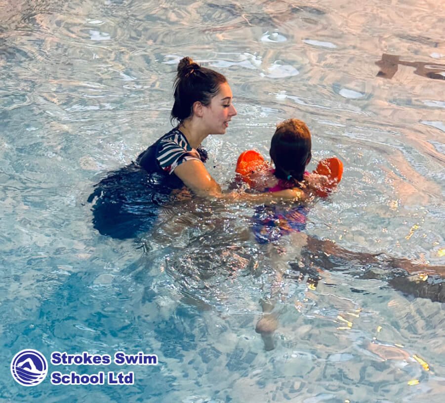 Instructor teaching girl with armbands in pool