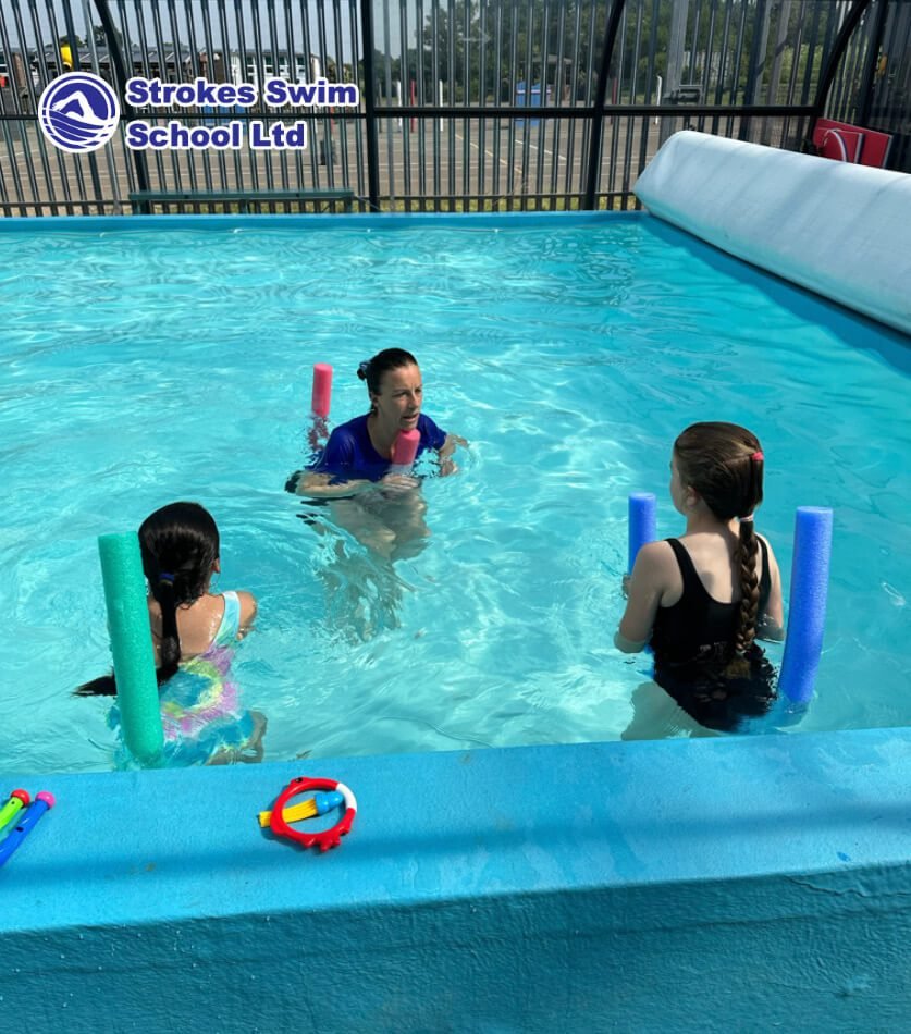 Swimming instructor teaching with noodles at outdoor pool