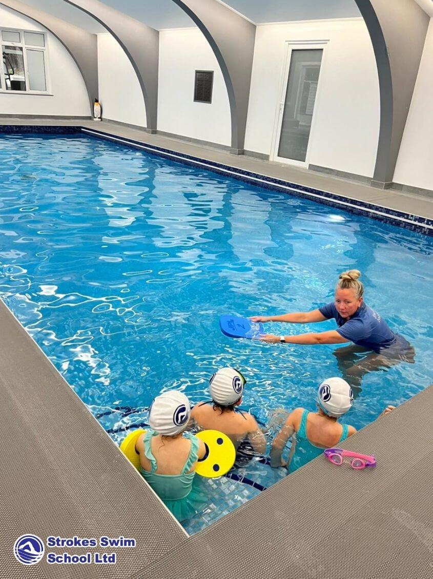 Swimming instructor teaching children in swim caps at Strokes Swim School