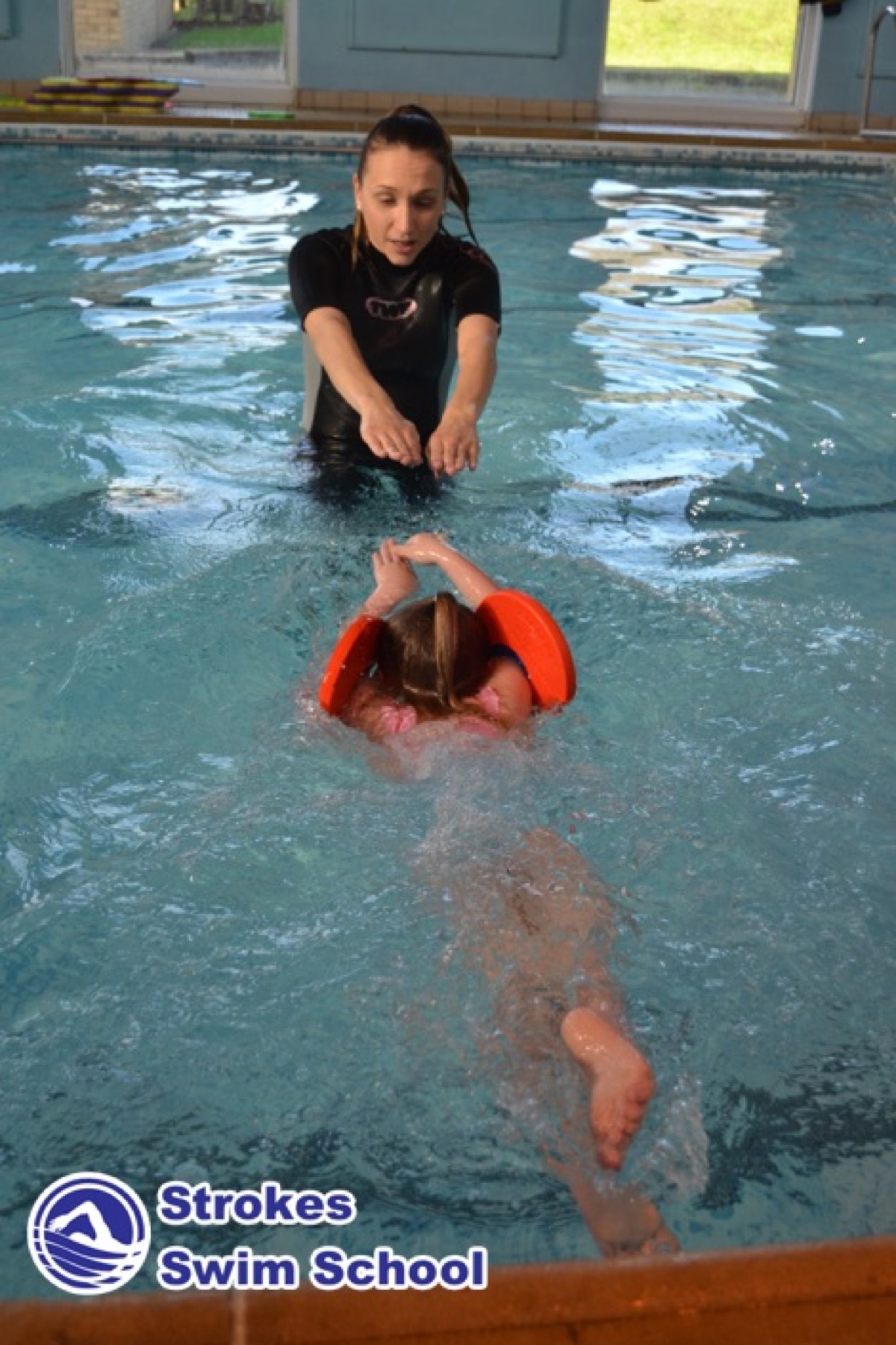 Swimming instructor teaching child with kickboard at Sweyne School